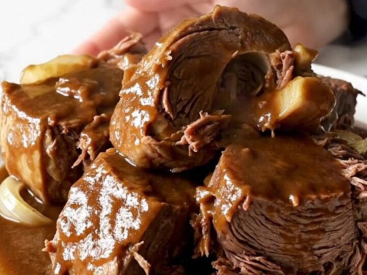 A close-up of a slow cooker filled with a tender beef chuck roast covered in a rich