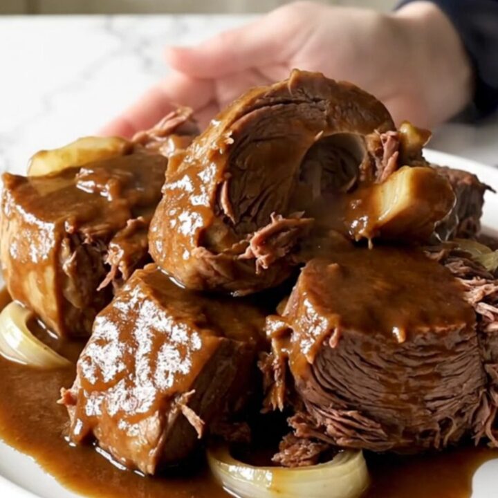 A close-up of a slow cooker filled with a tender beef chuck roast covered in a rich