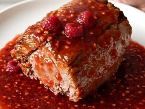 A close-up of a slow-cooked pork tenderloin smothered in a thick, glossy red raspberry pepper sauce.