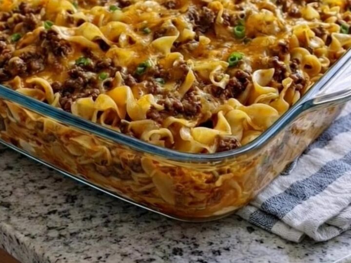 A steaming, golden-brown beef and noodle casserole in a glass dish with a melted cheese crust.
