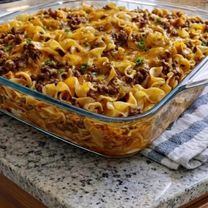 A steaming, golden-brown beef and noodle casserole in a glass dish with a melted cheese crust.