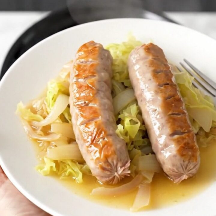 A top-down view of six raw bratwurst links arranged in a slow cooker with cabbage wedges and onions.