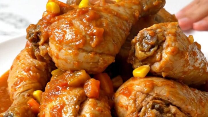 A rustic slow cooker filled with chicken thighs, corn, and peppers in a rich tomato sauce.