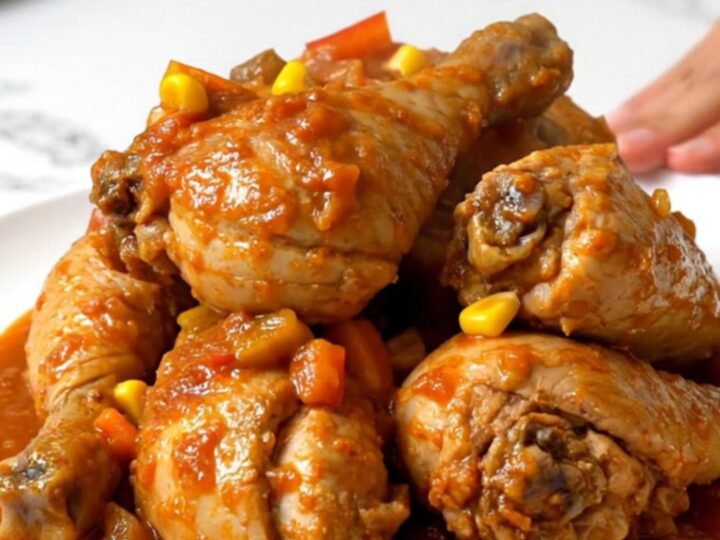 A rustic slow cooker filled with chicken thighs, corn, and peppers in a rich tomato sauce.