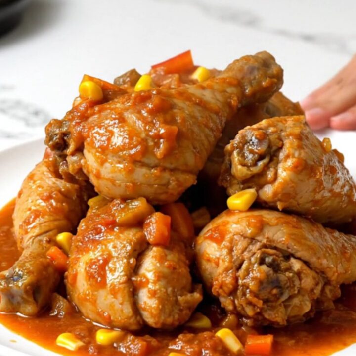 A rustic slow cooker filled with chicken thighs, corn, and peppers in a rich tomato sauce.