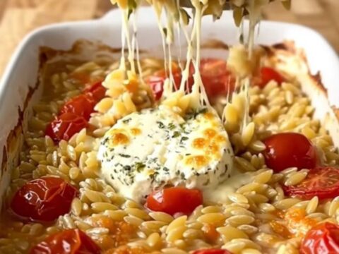 A large white rectangular baking dish filled with creamy baked orzo, burst cherry tomatoes