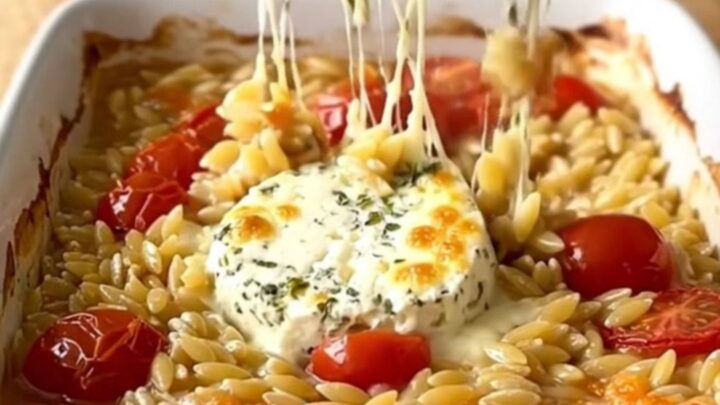 A large white rectangular baking dish filled with creamy baked orzo, burst cherry tomatoes
