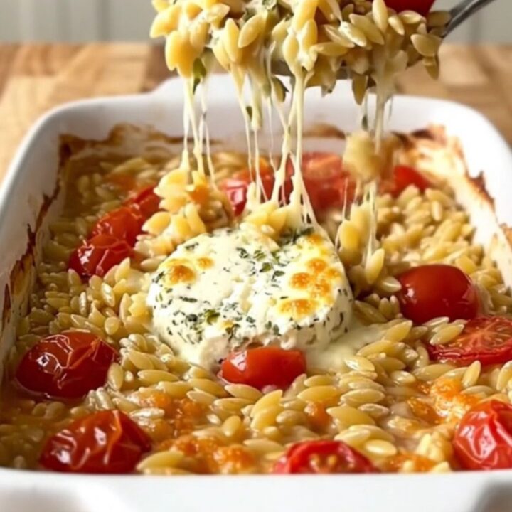 A large white rectangular baking dish filled with creamy baked orzo, burst cherry tomatoes