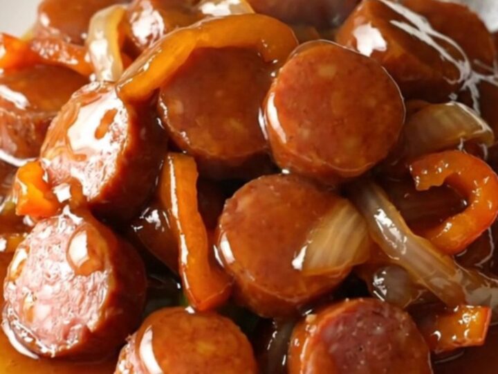 A close-up of Cajun honey smoked sausage coins with peppers and onions in a slow cooker.