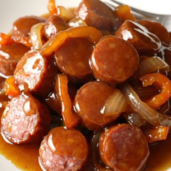 A close-up of Cajun honey smoked sausage coins with peppers and onions in a slow cooker.