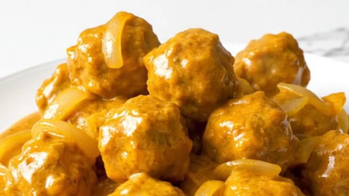 A close-up of tender chicken meatballs coated in a rich, creamy orange butter chicken sauce in a slow cooker.
