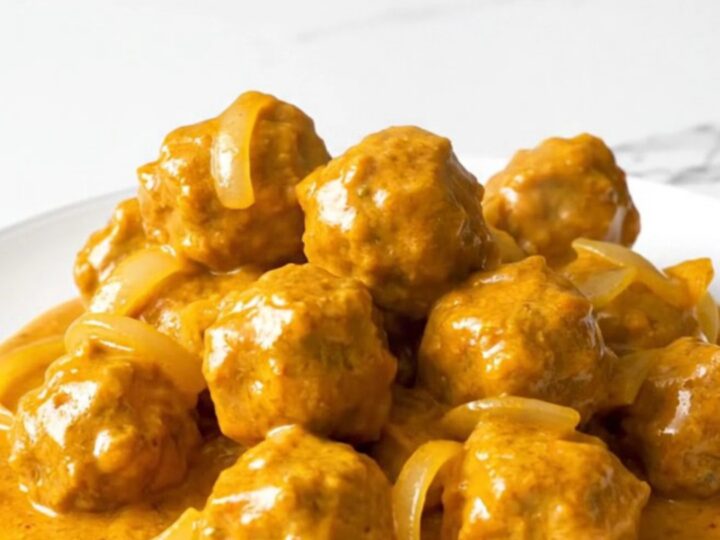 A close-up of tender chicken meatballs coated in a rich, creamy orange butter chicken sauce in a slow cooker.