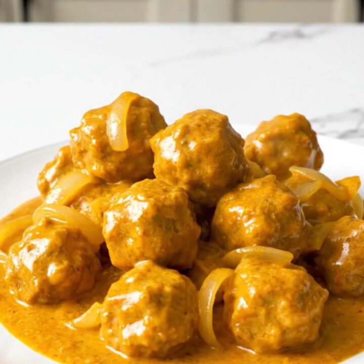 A close-up of tender chicken meatballs coated in a rich, creamy orange butter chicken sauce in a slow cooker.