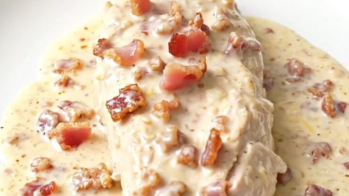 A close-up of tender chicken breasts in a creamy parmesan and bacon sauce inside a slow cooker.