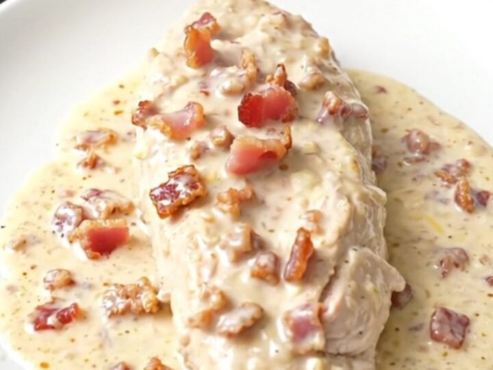 A close-up of tender chicken breasts in a creamy parmesan and bacon sauce inside a slow cooker.