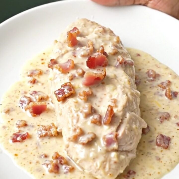 A close-up of tender chicken breasts in a creamy parmesan and bacon sauce inside a slow cooker.