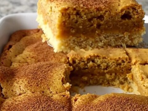A golden-brown pumpkin gooey butter bar lifted by a spatula, showing a soft, moist center.