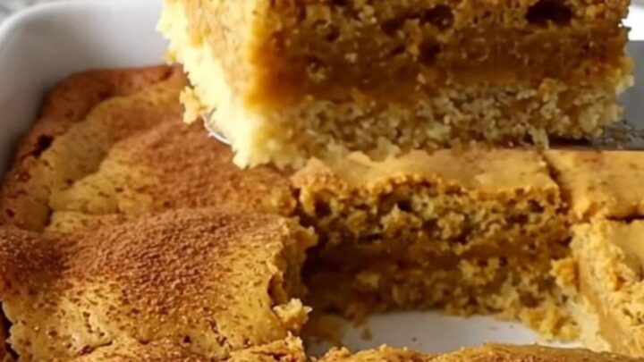 A golden-brown pumpkin gooey butter bar lifted by a spatula, showing a soft, moist center.