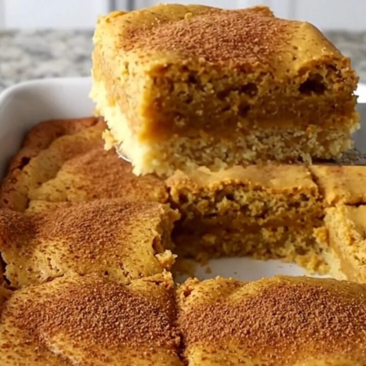 A golden-brown pumpkin gooey butter bar lifted by a spatula, showing a soft, moist center.