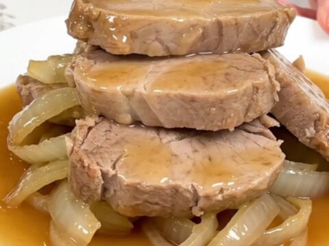 Slow cooker honey ginger pork tenderloin served on a white plate with soft onions and sauce.