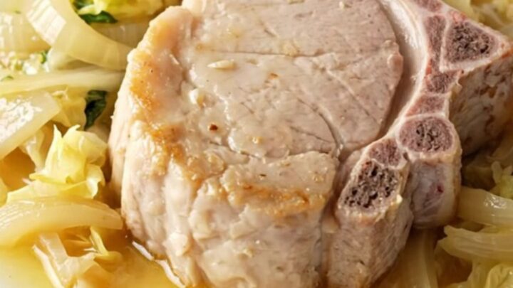 A high-angle view of raw pork chops, cabbage wedges, and sliced onions arranged in a stoneware slow cooker.
