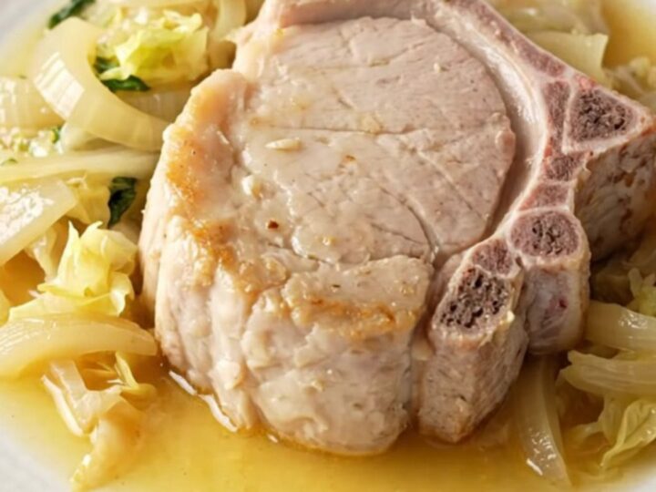 A high-angle view of raw pork chops, cabbage wedges, and sliced onions arranged in a stoneware slow cooker.