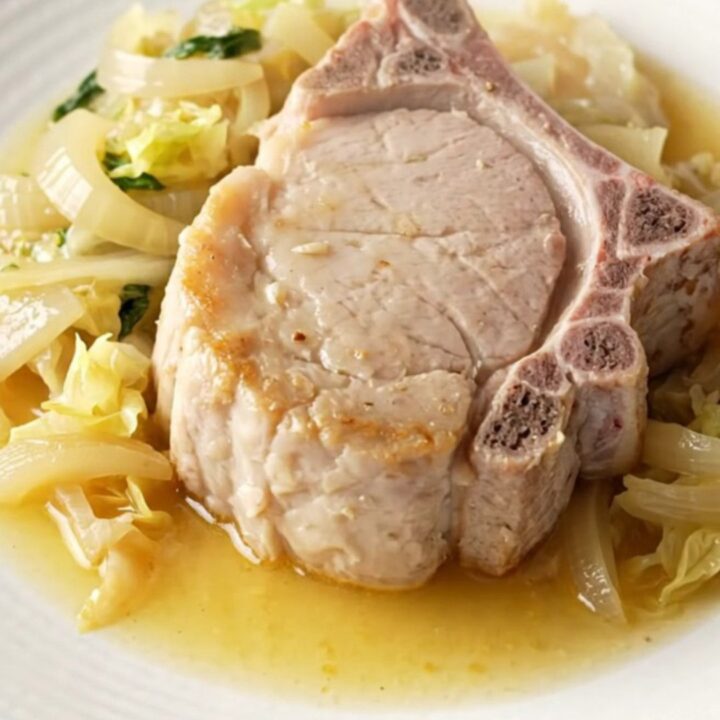 A high-angle view of raw pork chops, cabbage wedges, and sliced onions arranged in a stoneware slow cooker.