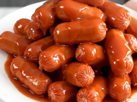 A slow cooker filled with glistening, maple sriracha glazed cocktail smokies ready for serving.