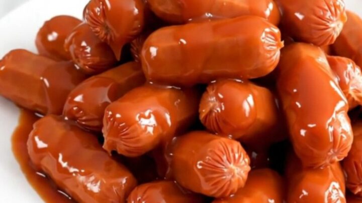 A slow cooker filled with glistening, maple sriracha glazed cocktail smokies ready for serving.