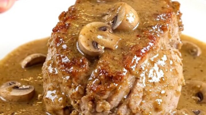 A whole slow-cooked pork tenderloin smothered in a creamy marsala mushroom sauce on a white plate.