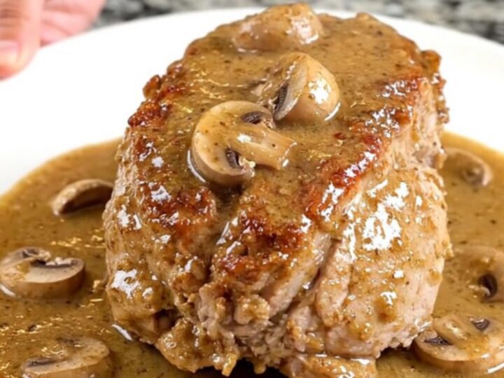 A whole slow-cooked pork tenderloin smothered in a creamy marsala mushroom sauce on a white plate.