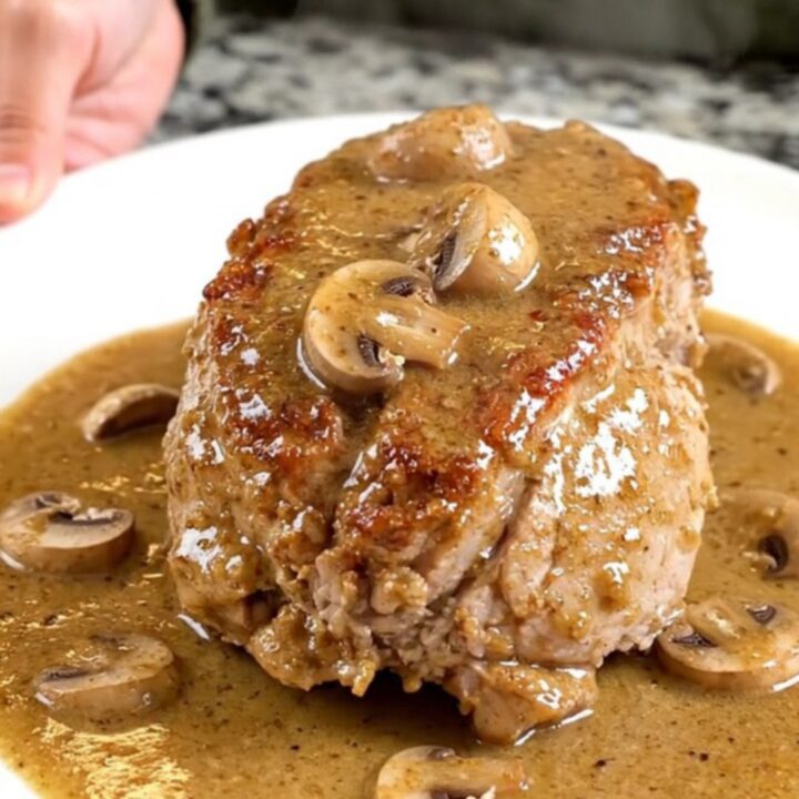 A whole slow-cooked pork tenderloin smothered in a creamy marsala mushroom sauce on a white plate.