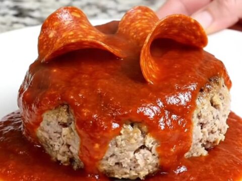 A close-up view of cooked turkey burger steaks in a slow cooker topped with marinara and pepperoni.