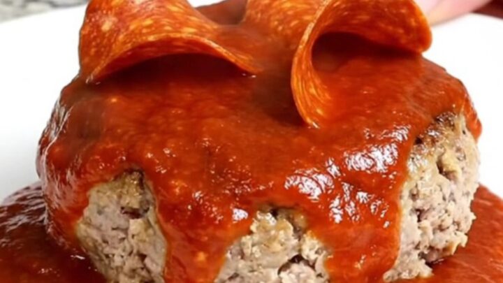 A close-up view of cooked turkey burger steaks in a slow cooker topped with marinara and pepperoni.
