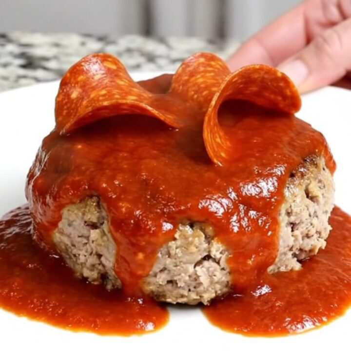 A close-up view of cooked turkey burger steaks in a slow cooker topped with marinara and pepperoni.
