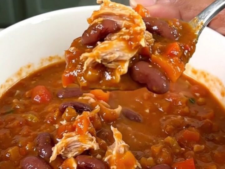 A top-down view of a black slow cooker filled with a steaming, hearty Cajun turkey chili with beans.