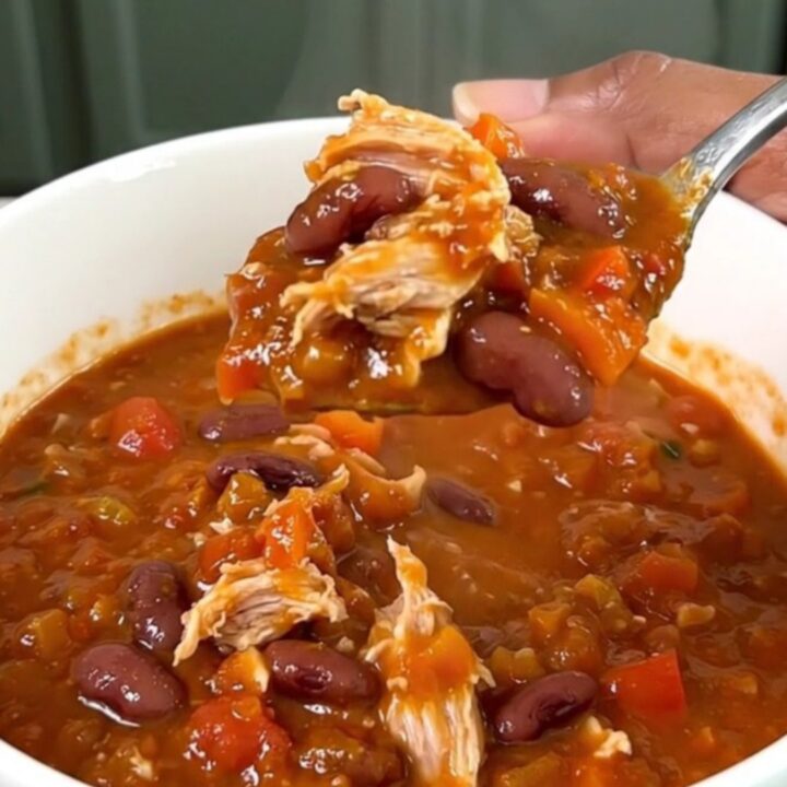 A top-down view of a black slow cooker filled with a steaming, hearty Cajun turkey chili with beans.
