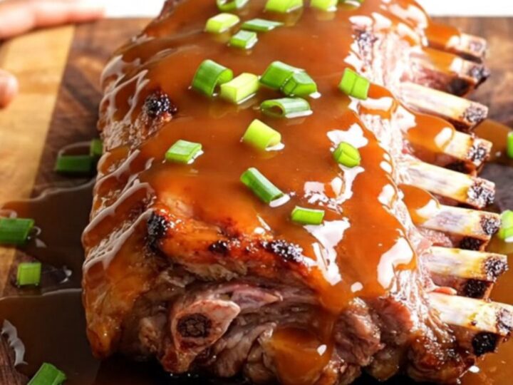 A close-up of tender, glazed honey sriracha baby back ribs arranged on a wooden serving board.