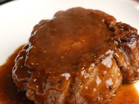 A close-up of a bone-in pork shoulder steak coated in a thick, glossy BBQ sauce inside a black slow cooker.