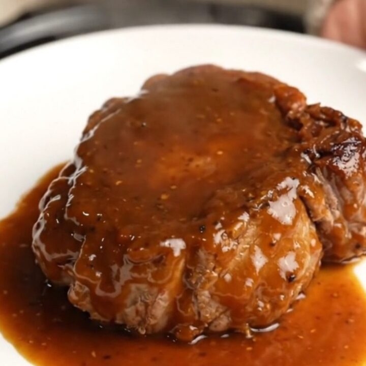 A close-up of a bone-in pork shoulder steak coated in a thick, glossy BBQ sauce inside a black slow cooker.