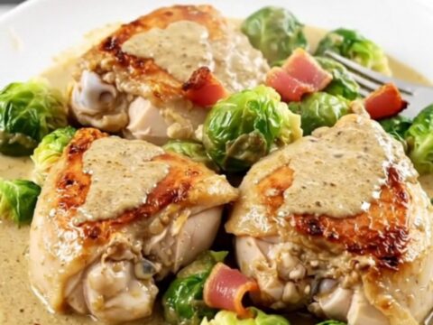 A top-down view of creamy slow cooker chicken thighs with bacon and Brussels sprouts in a black slow cooker.