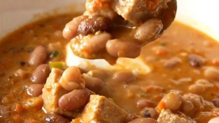 A bowl of creamy white pork chili featuring tender pork chunks, white beans, and a garnish of herbs.