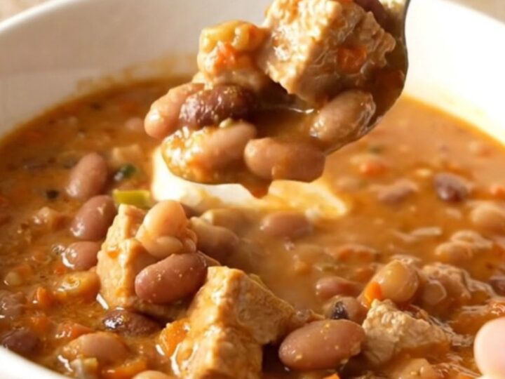 A bowl of creamy white pork chili featuring tender pork chunks, white beans, and a garnish of herbs.