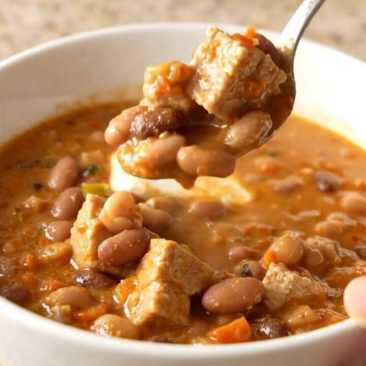 A bowl of creamy white pork chili featuring tender pork chunks, white beans, and a garnish of herbs.