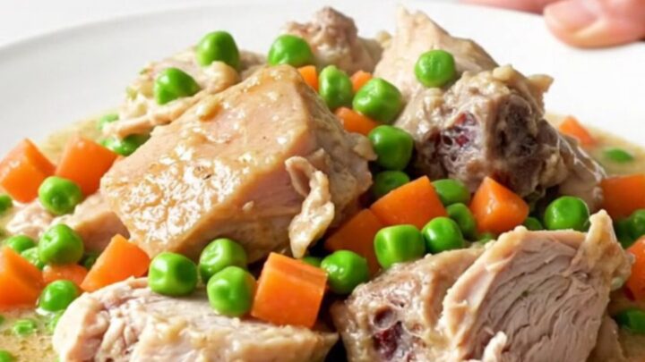 A white plate filled with creamy turkey a la king, featuring visible chunks of turkey, peas, and carrots in a rich sauce.