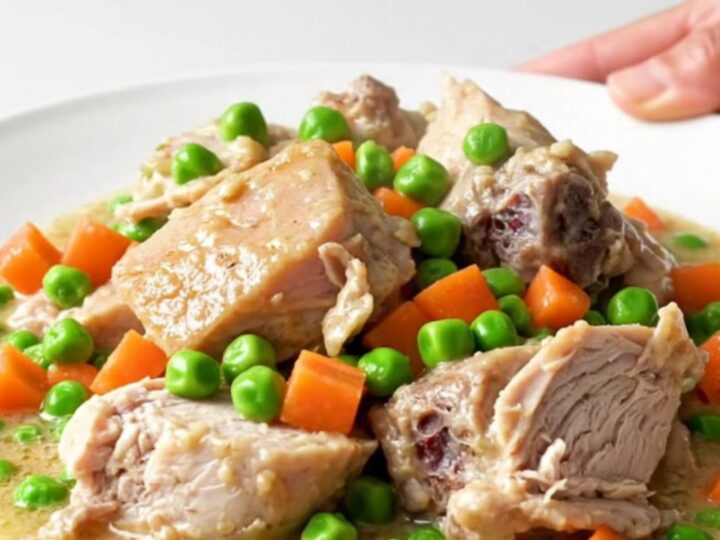 A white plate filled with creamy turkey a la king, featuring visible chunks of turkey, peas, and carrots in a rich sauce.