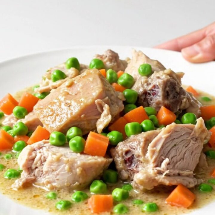 A white plate filled with creamy turkey a la king, featuring visible chunks of turkey, peas, and carrots in a rich sauce.