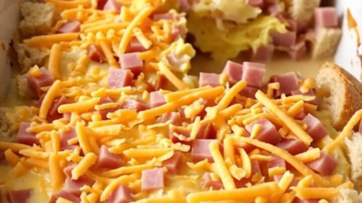 A golden-brown ham and cheddar breakfast strata in a white baker on a speckled countertop.