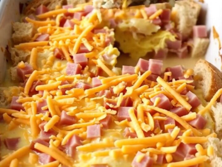 A golden-brown ham and cheddar breakfast strata in a white baker on a speckled countertop.