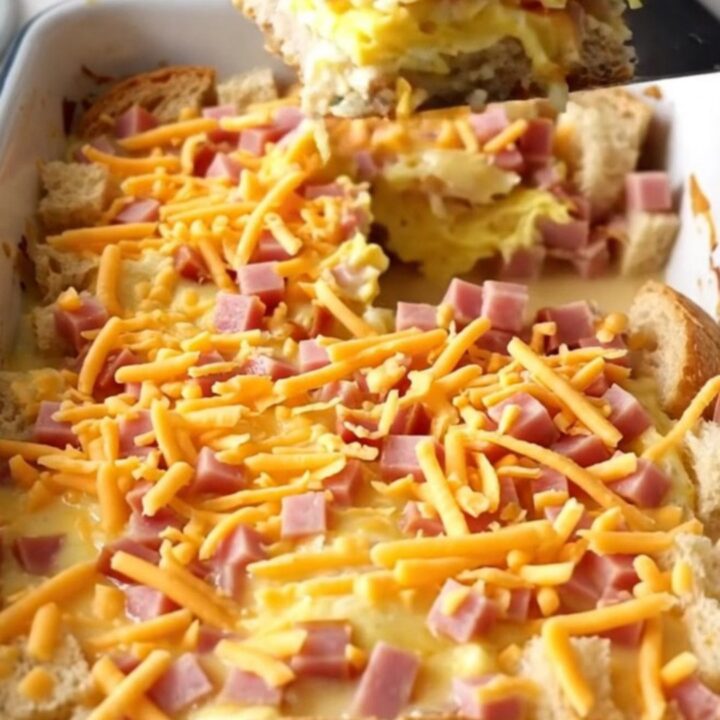 A golden-brown ham and cheddar breakfast strata in a white baker on a speckled countertop.